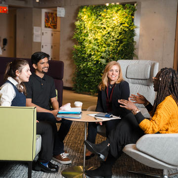 Four people having a conversation in chairs in Gutman Library